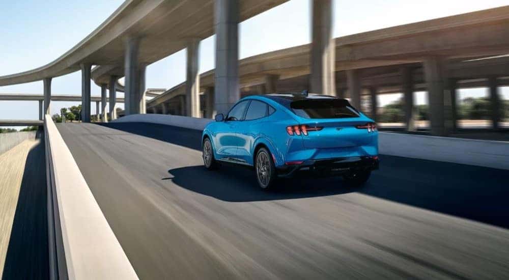 A blue 2022 Ford Mustang Mach-E is shown driving near an overpass.
