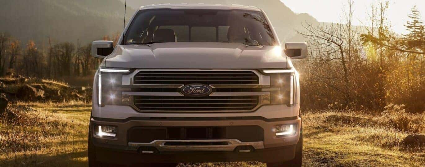 A white 2024 Ford F-150 King Ranch is shown from the front parked on a remote trail.