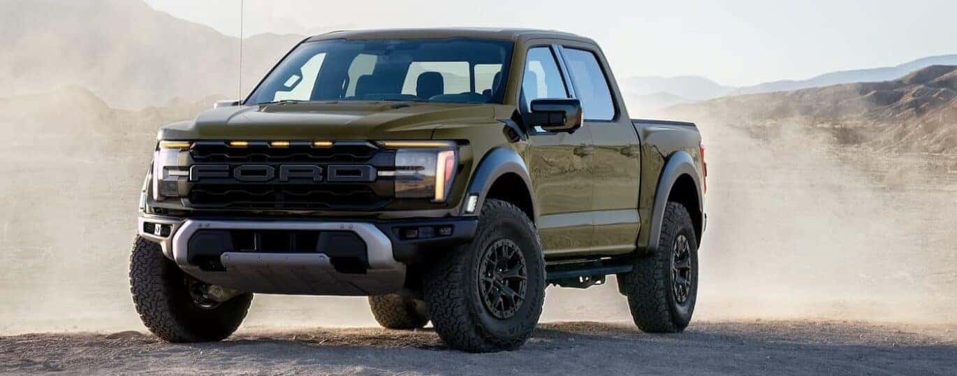 A green 2024 Ford F-150 Raptor is shown parked in a dusty area.