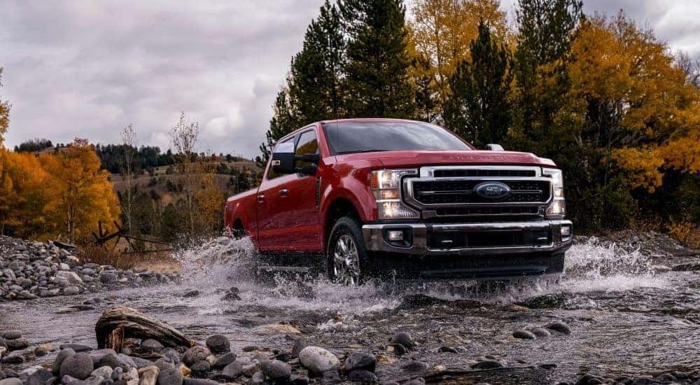 A red 2021 Ford F-250 is shown splashing through a creek.