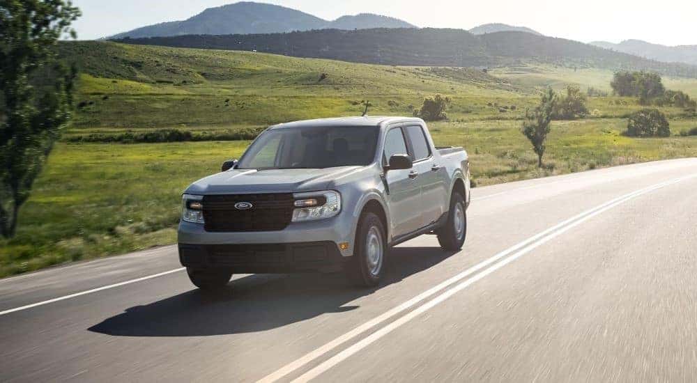 A grey 2022 Ford Maverick is shown driving on an open road after looking at used trucks for sale near Colonie.