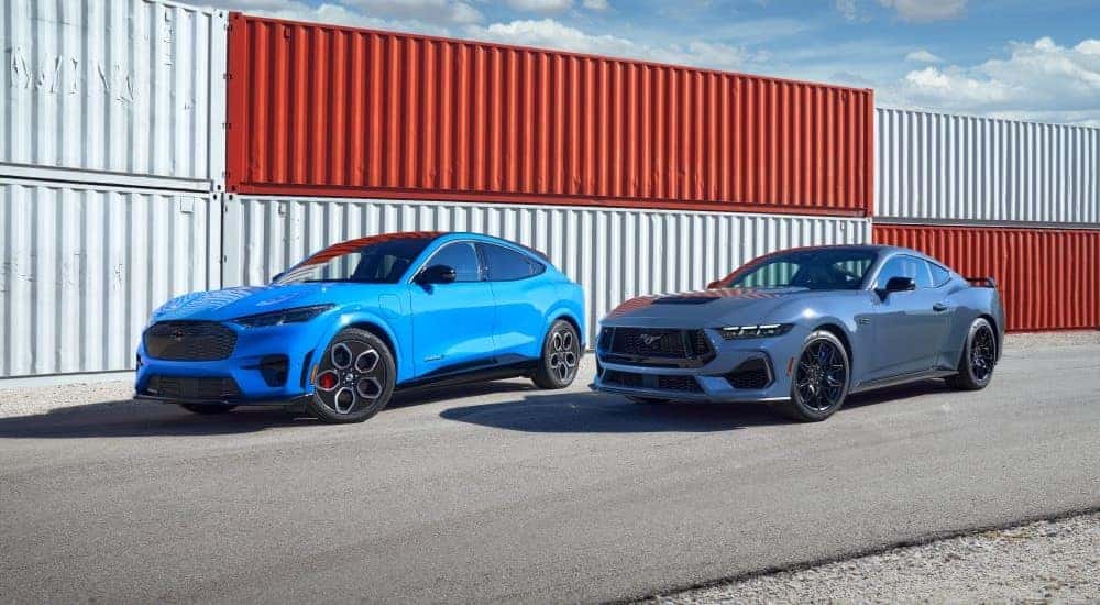 A pair of blue 2024 Ford Mustang Mach-E's are shown parked near shipping containers.