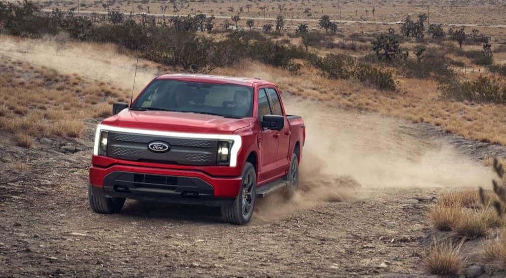 A red 2024 Ford F-150 Lightning is shown driving off-road.