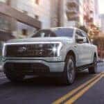 A white 2023 Ford F-150 Lightning is shown driving from a Ford EV dealership near Catskill.