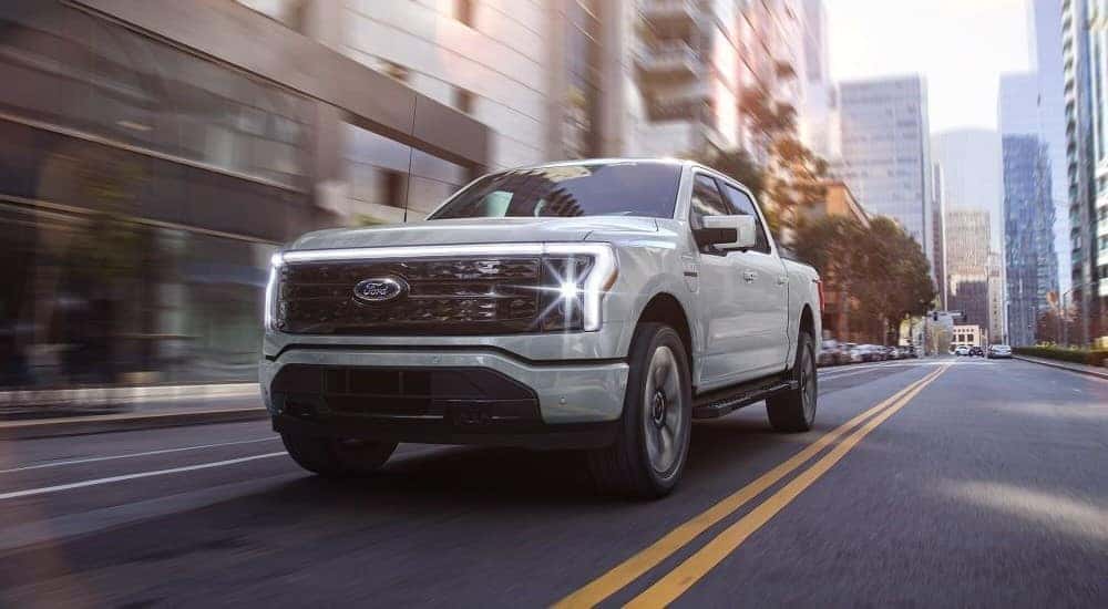 A white 2024 Ford F-150 Lightning is shown driving from a Ford EV dealership near Catskill.