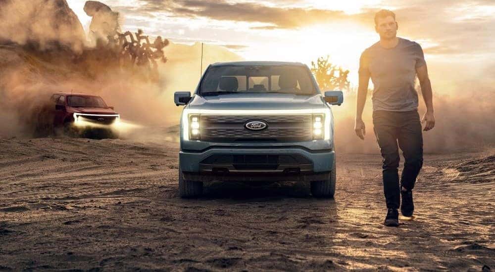 A man is shown walking away from a blue 2024 Ford F-150 Lightning parked off-road.