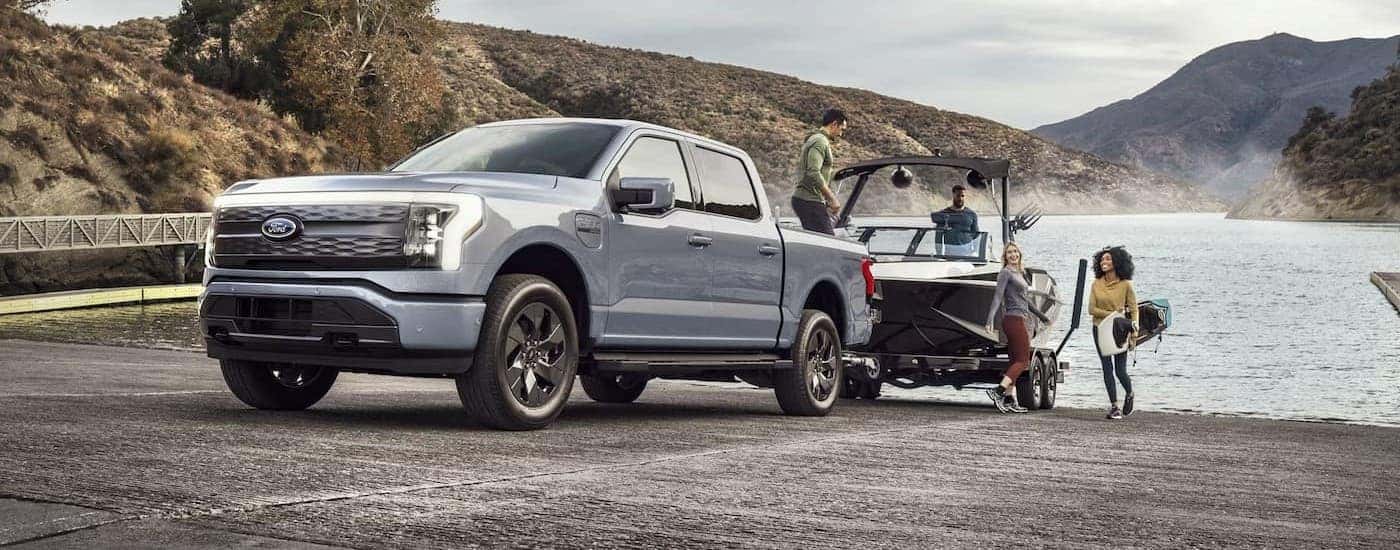 A silver 2023 Ford F-150 Lightning is shown towing a boat.