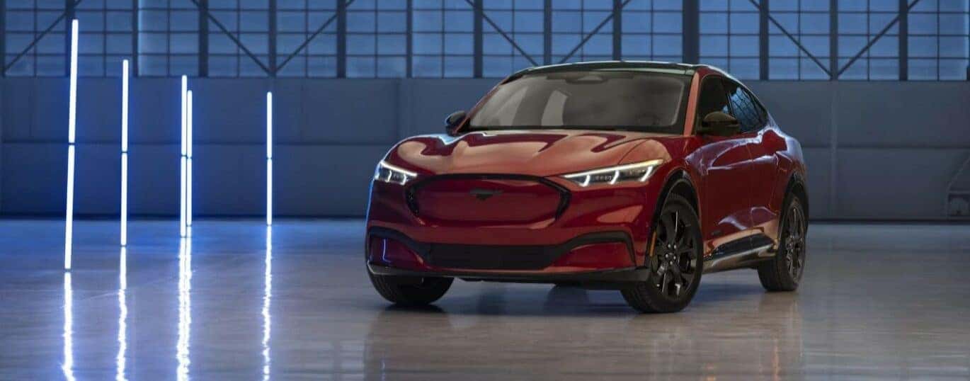 A red 2024 Ford Mustang Mach-E is shown parked in a garage during a 2024 Ford Mustang Mach-E vs 2024 Nissan ARIYA..