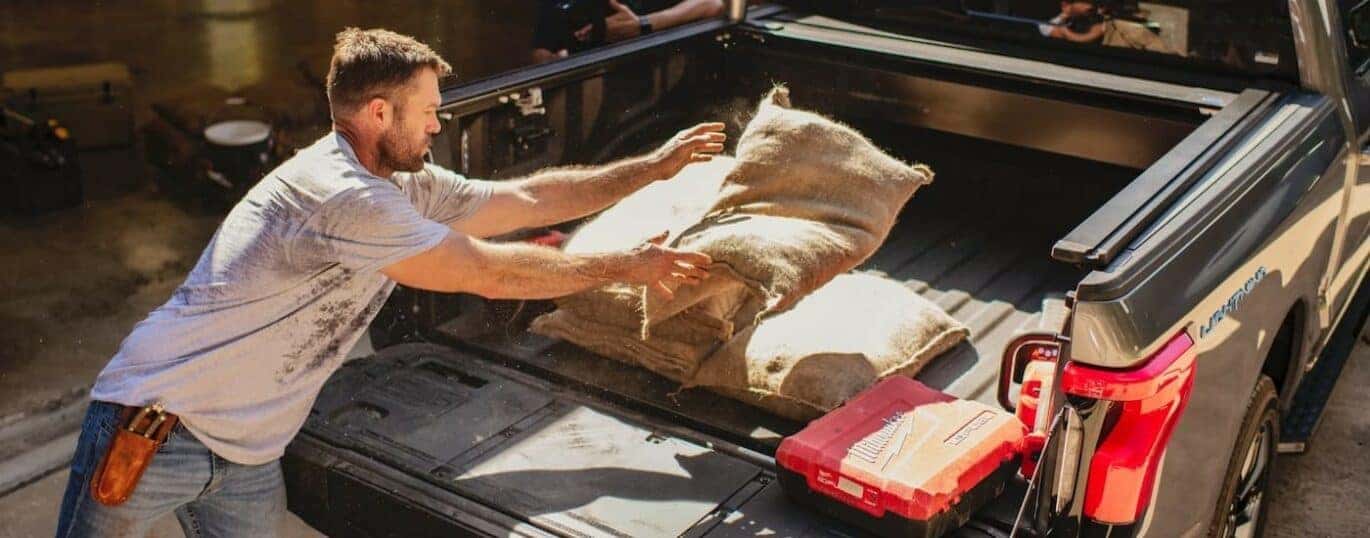 A person is shown throwing a sack into the bed of a silver 2024 Ford F-150 Lightning.