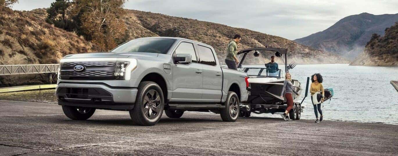 After competing in a 2024 Ford F-150 Lightning vs 2024 Tesla Cybertruck comparison, a silver 2024 Ford F-150 Lightning, is shown towing a boat.