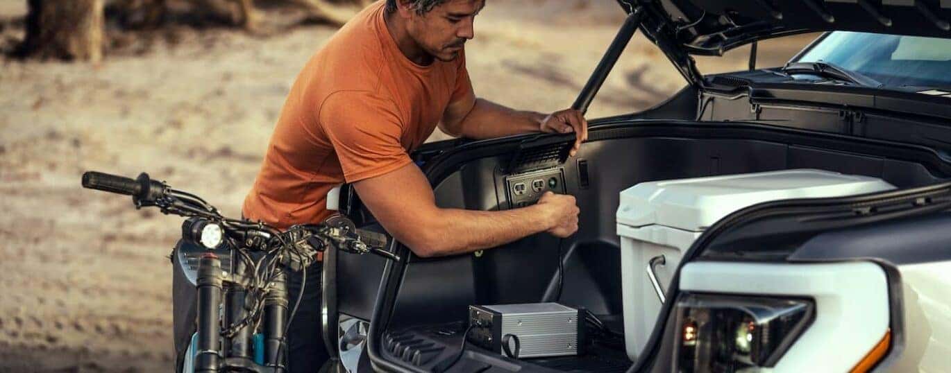 A person is shown using an outlet in the frunk of a silver 2024 Ford F-150 Lightning.