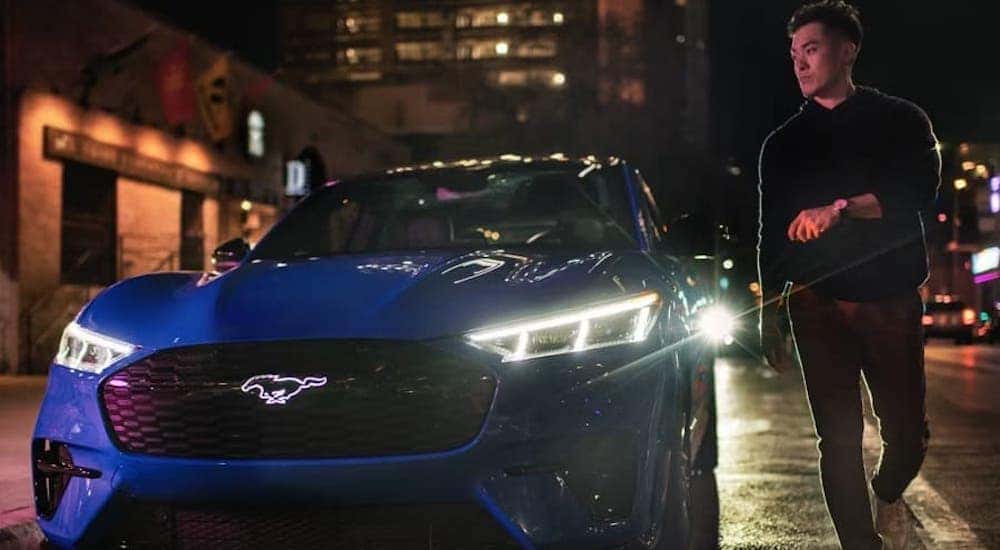 A man is shown walking near a blue 2024 Ford Mustang Mach-E parked by a curb.