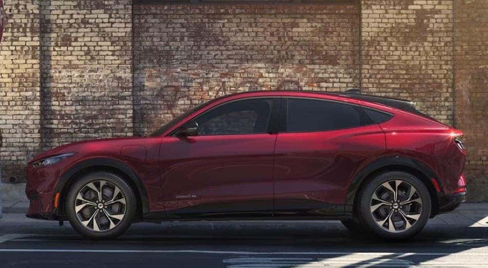 A red 2024 Ford Mustang Mach-E is shown from a side angle while parked outside a building.