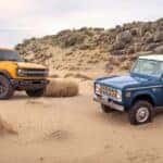 A yellow 2021 Ford Bronco and a blue 1966 Ford Bronco parked in sand outside a used Ford dealership near Halfmoon.