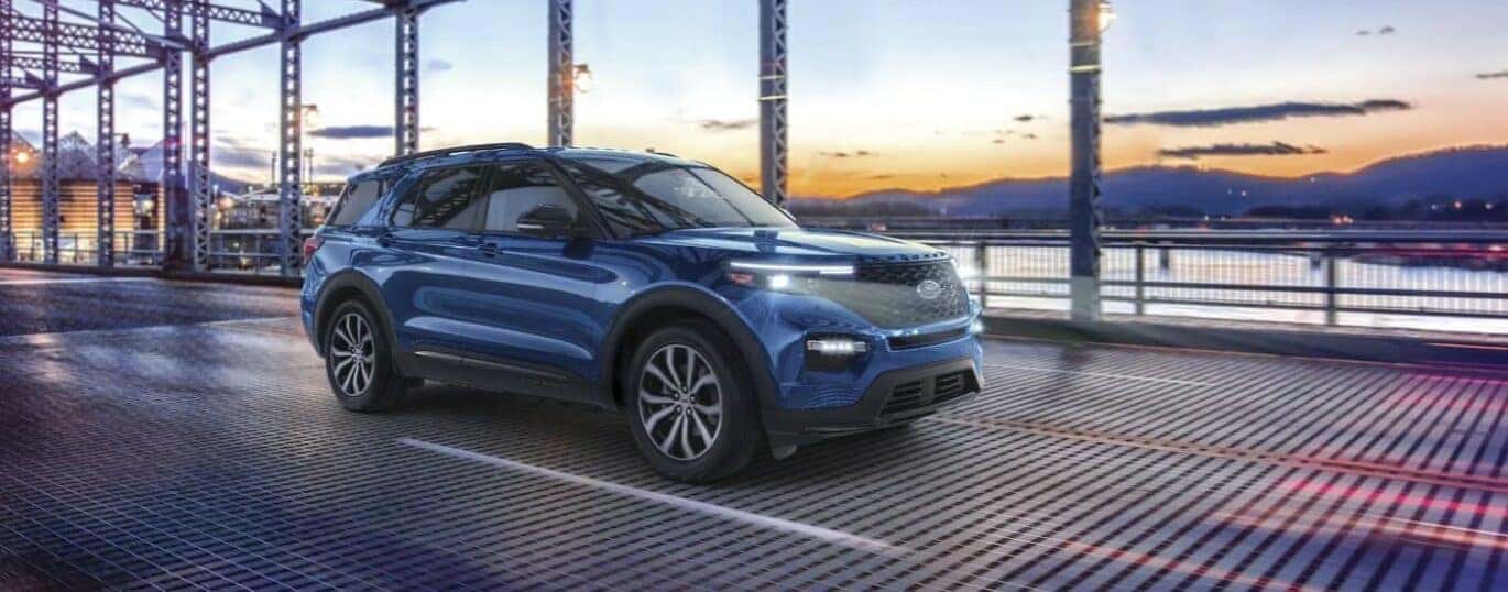 A blue 2024 Ford Explorer is shown driving on a bridge.