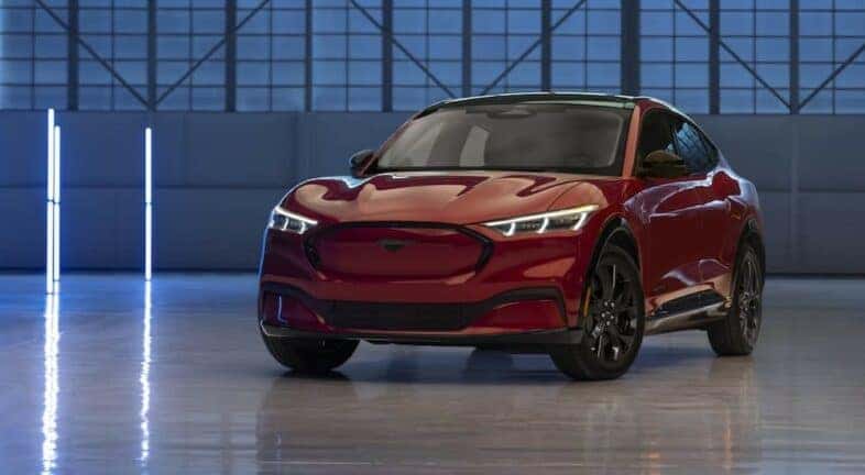 A red 2023 Ford Mustang Mach-E is shown parked on a warehouse floor.