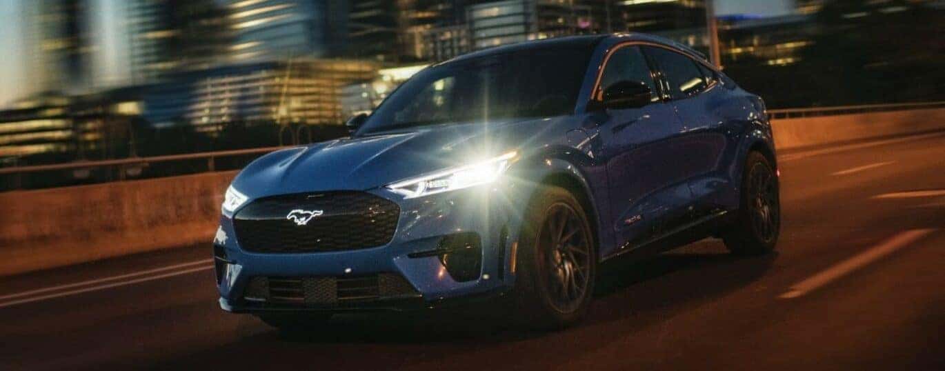 A blue 2024 Ford Mustang Mach-E is shown driving at night.