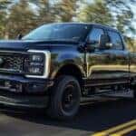 A black 2024 Ford Super Duty F-250 driving on an open road.