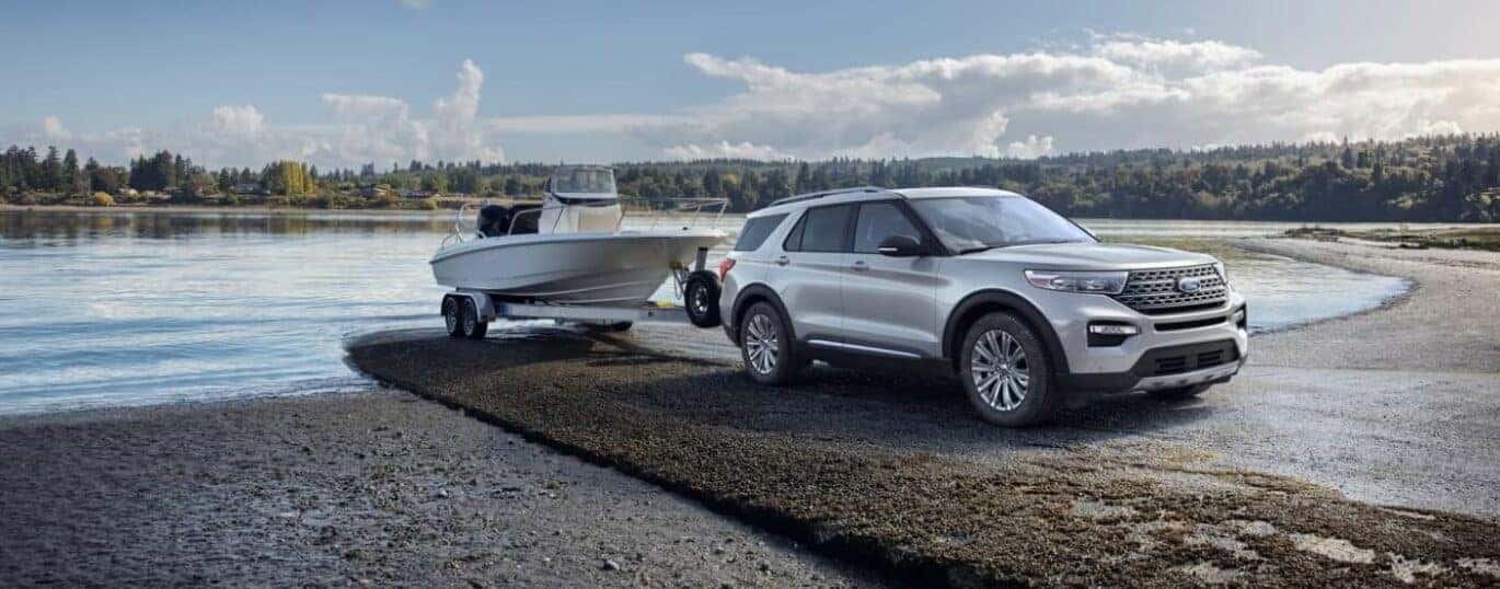 A white 2024 Ford Explorer is shown towing a boat out of a lake.