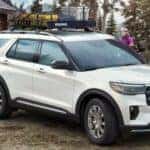 A white 2025 Ford Explorer is shown parked near a log cabin.
