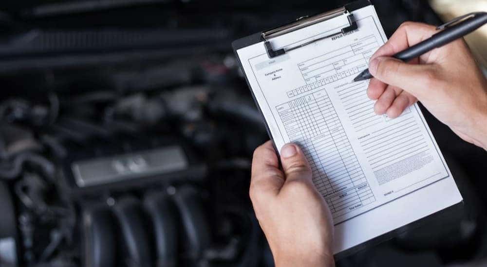 A mechanic is shown holding a clipboard near an engine bay.