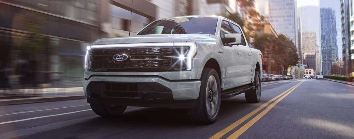 A white 2024 Ford F-150 Lightning driving in a city.
