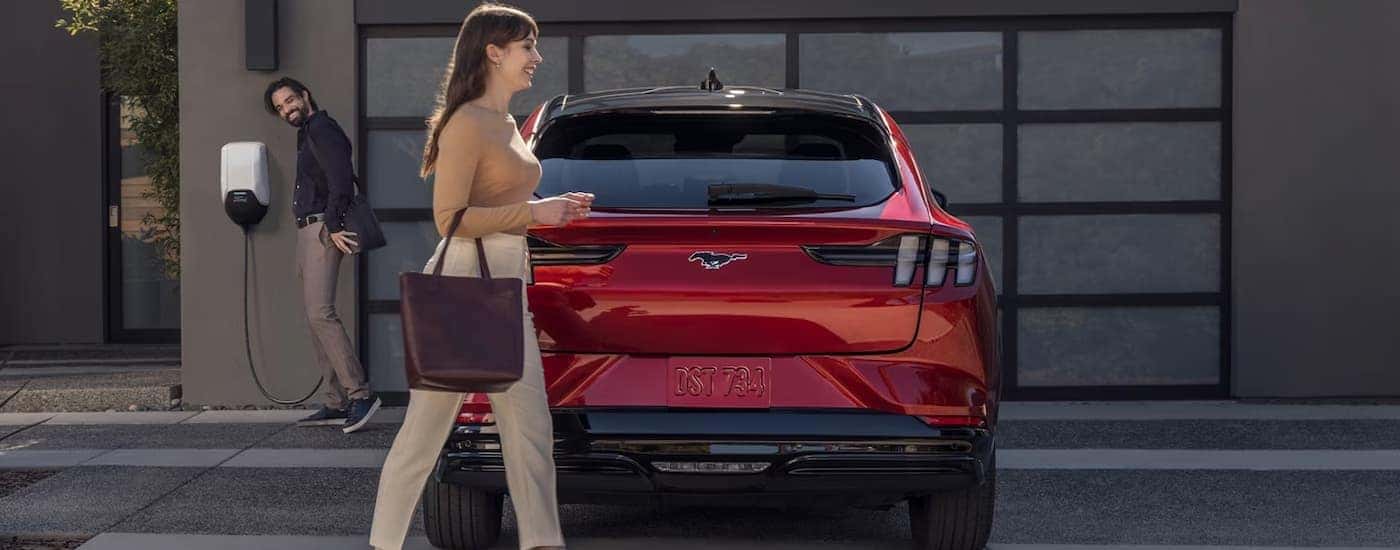 A red 2023 Ford Mustang Mach-E is parked in a driveway while charging.