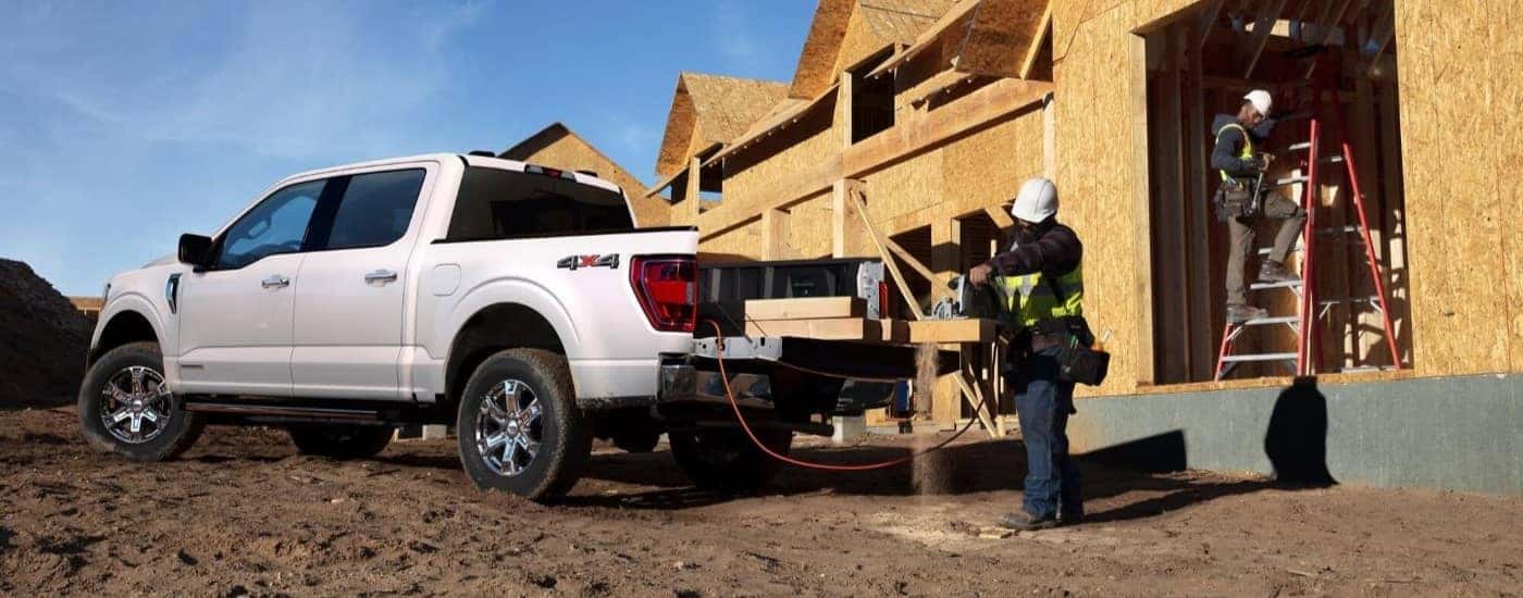 Construction workers cutting boards in the bed of a white 2022 Ford F-150.