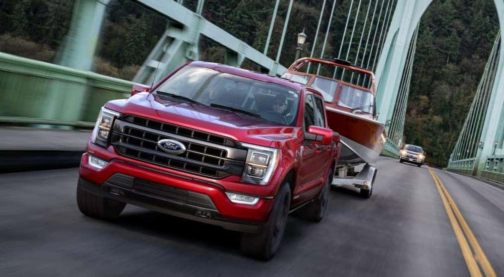A red 2021 Ford F-150 is shown towing a boat across a bridge.
