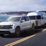 A white 2024 Ford F-150 Lightning towing a trailer.
