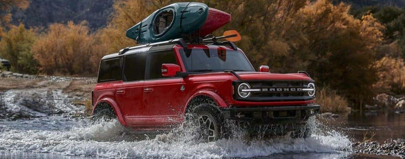 A red 2024 Ford Bronco Outer Banks driving over a shallow pond.