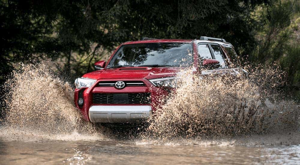A red 2024 Toyota 4Runner TRD Off-Road driving through a muddy puddle.
