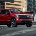 A red 2024 Ford F-150 Lightning for sale is shown parked near a person walking.