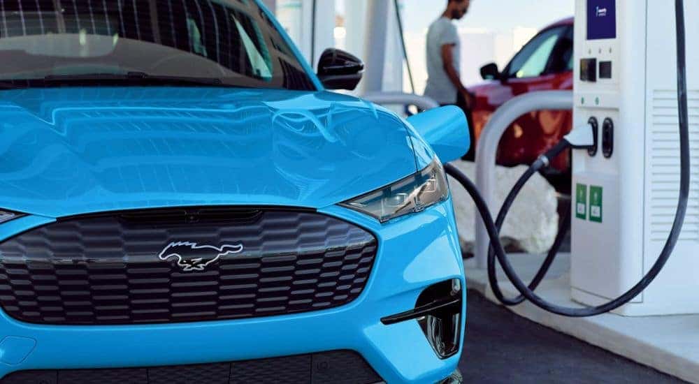 A close up shows a blue 2024 Ford Mustang Mach-E at a charging station.