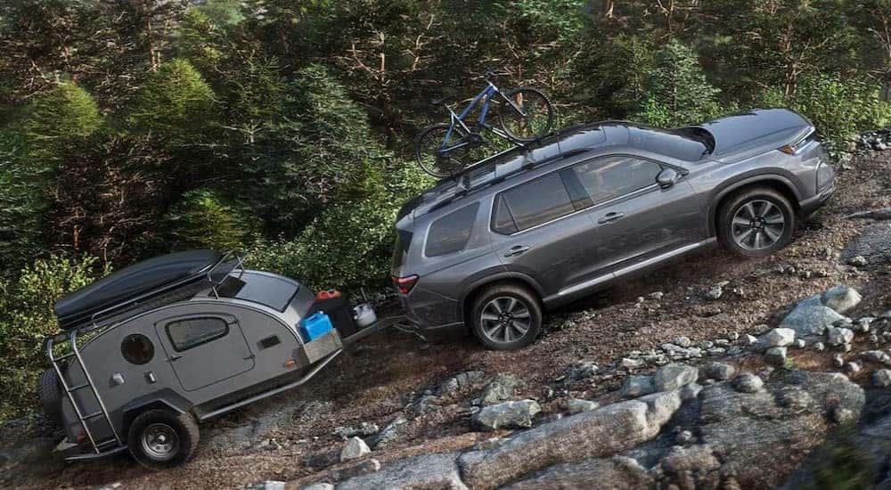 A gray 2025 Honda Pilot is shown towing a trailer off-road.