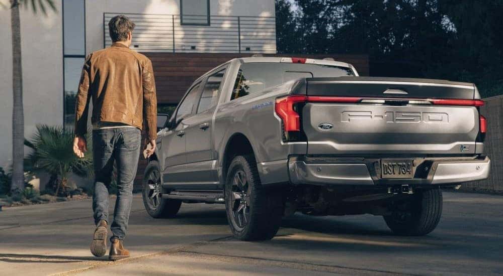 A person walking towards a grey 2024 Ford F-150 Lightning parked in a driveway.