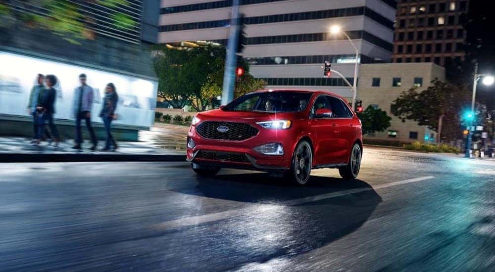 A red 2023 Ford Edge ST driving through a city at night.