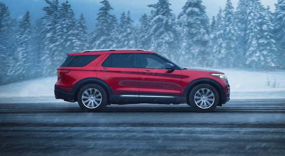 A side view of a red 2023 Ford Explorer Limited driving down a snowy road.