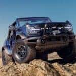 A blue 2021 Ford Bronco driving over a rocky desert cliff.