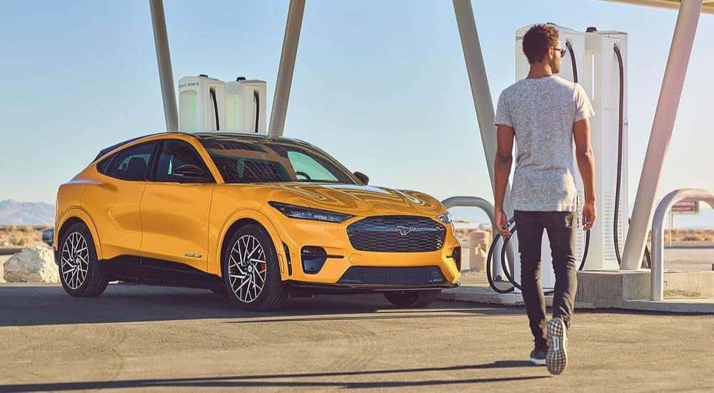 A person walking towards a yellow 2024 Ford Mustang Mach-E GT parked at a charging station.