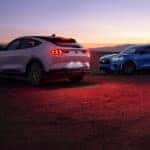 Two 2024 Ford Mustang Mach-E SUVs parked in the desert with their lights on at night.