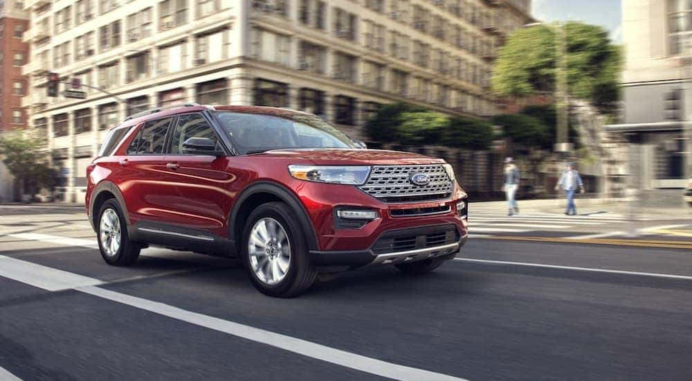 A red 2020 Ford Explorer driving from a dealer with a used Ford Explorer for sale.
