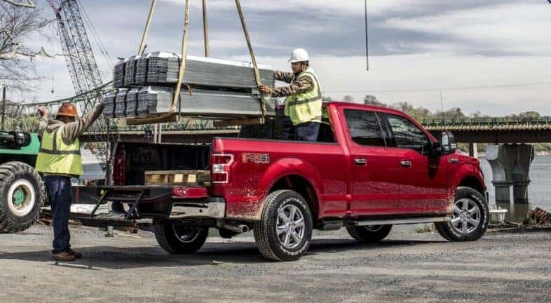 A popular used Ford F-150 for sale near Troy, a red 2020 Ford F-150, is shown having materials loaded into the bed.