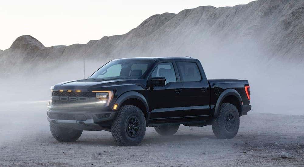A black 2021 Ford F-150 Raptor angled left while off-roading in a desert.