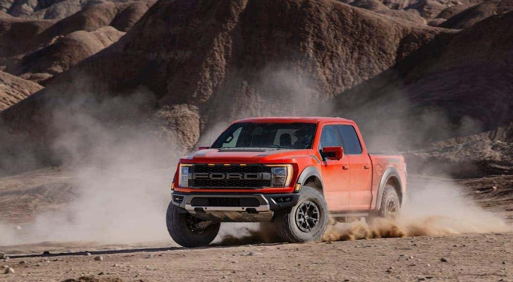 Wide angle shot of a red 2021 Ford F-150 Raptor off-roading in a desert.