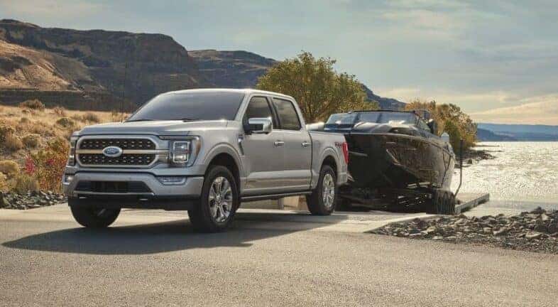 A popular used Ford F-150 for sale in Albany, a silver 2023 Ford F-150, is shown towing a boat.