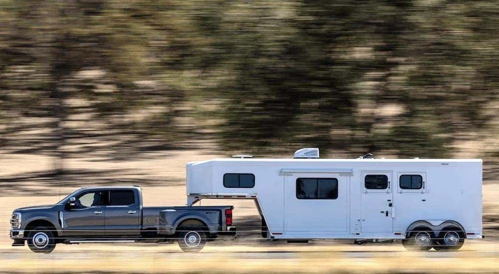 A grey 2024 Ford F-350 Lariat is shown from the side while towing a trailer.