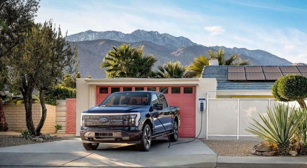 A black 2022 Ford F-150 Lightning plugged into a home charger in a driveway.