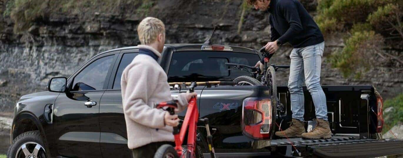 Two people are shown loading bicycles onto the bed of a 2024 Ford Ranger XLT.