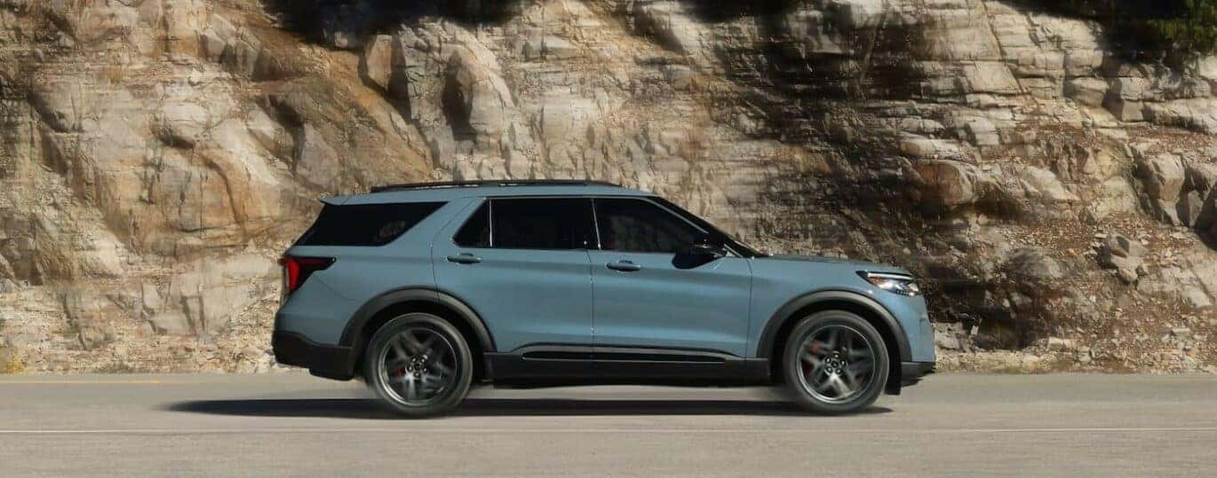 A blue 2024 Ford Explorer is shown driving on a highway.